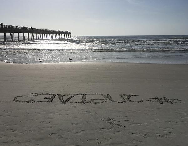 Hashtag JU Gives written in the sand.